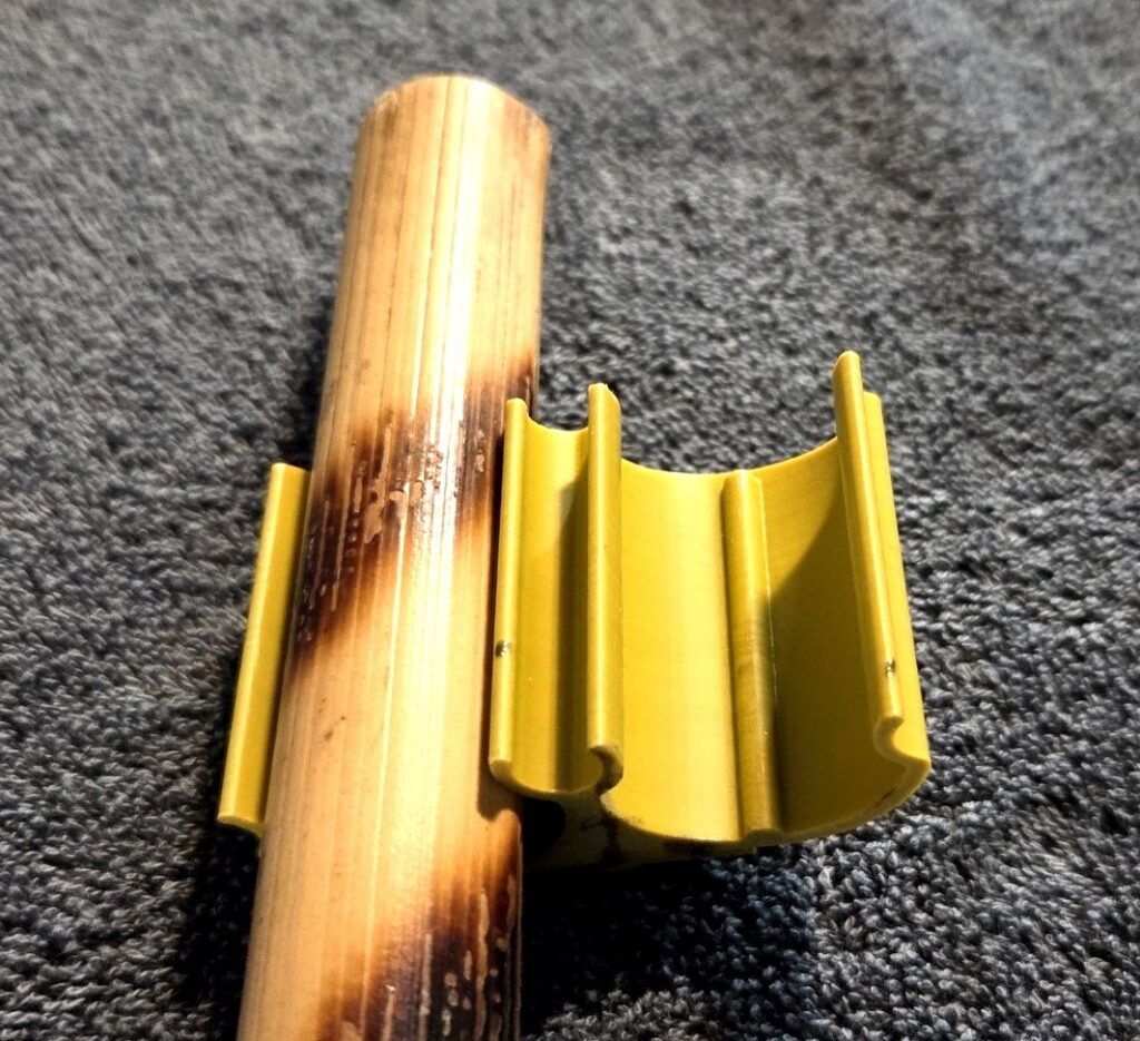 The Kali Klip prototype securely holding a rattan stick, displayed on a gray textured surface